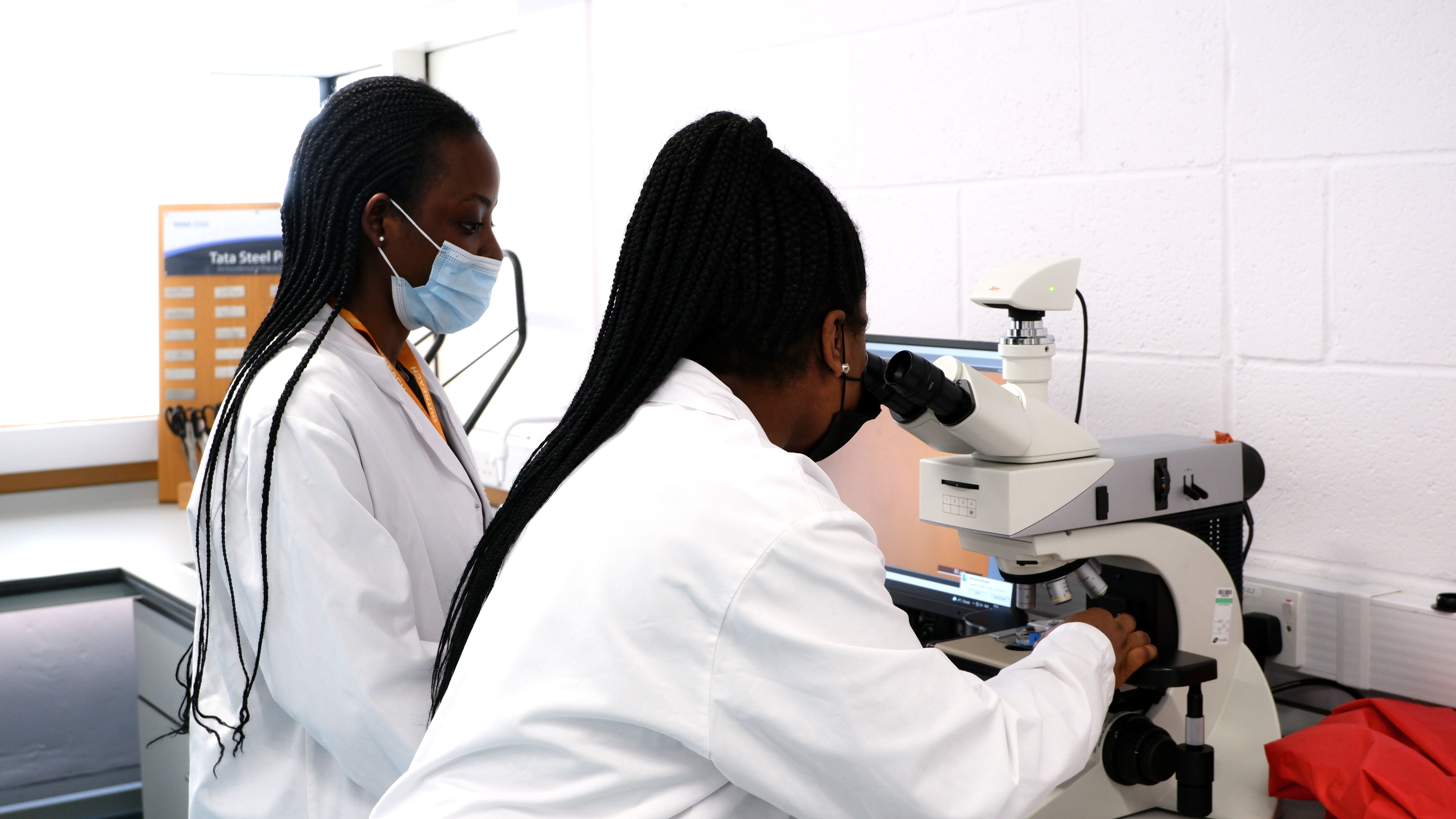 a photo of two girls wearing lab coats looking at a microscope