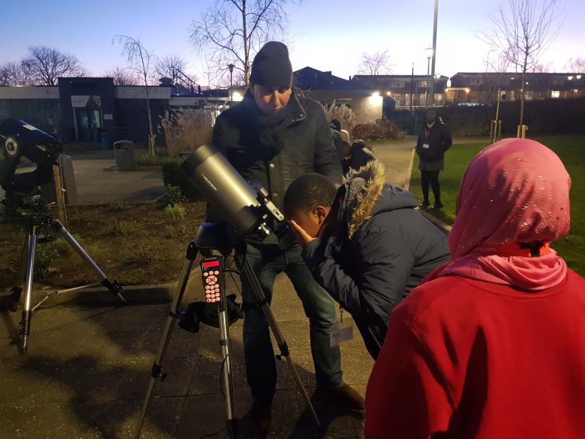 Young people peering through telescope 