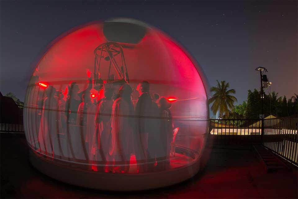 Female students in a red bubble with Professor Katherine Blundell looking up at the night sky through a telescope