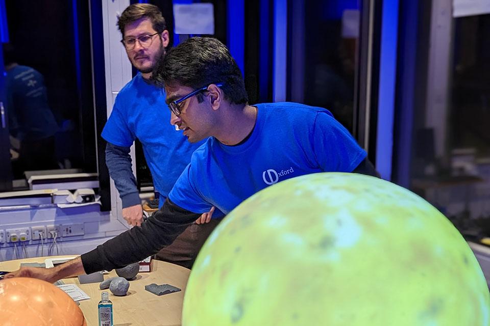 A planet in the foreground and two male scientists in the background