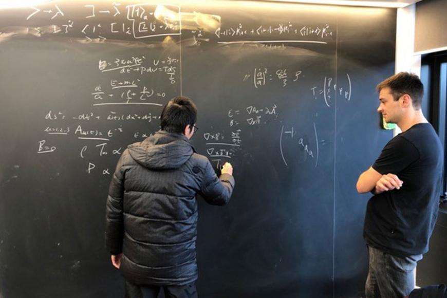 Two males standing in front of a blackboard with equations written on it