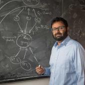 Professor Siddharth Parameswaran in front of a black chalk board