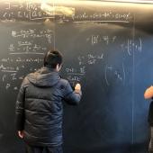 Two males standing in front of a blackboard with equations written on it