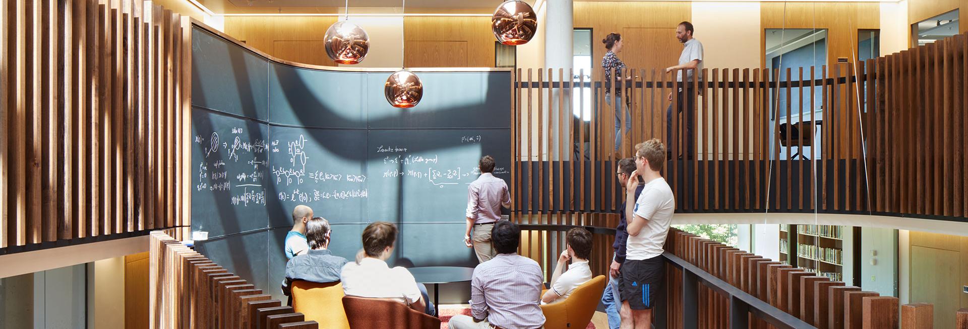 A group of researchers talking through a problem on a blackboard in the Beecroft building, Department of Physics