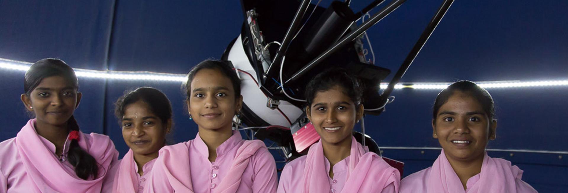Girls in India standing in front of a telescope
