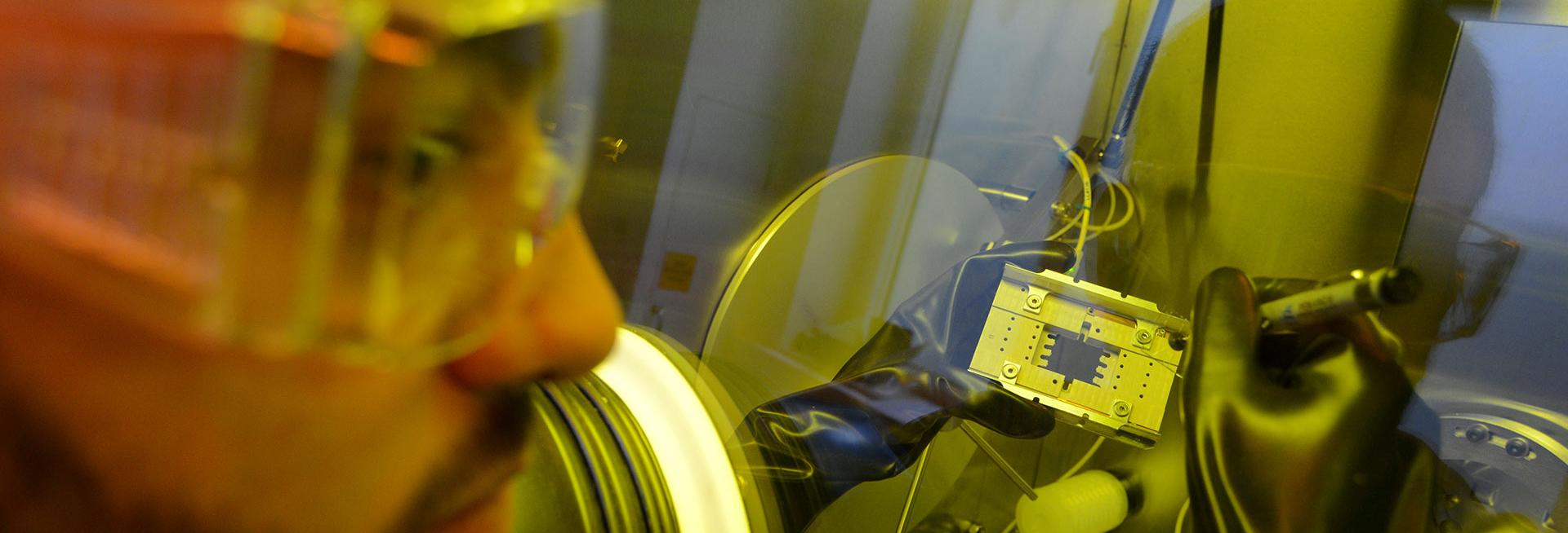 Man wearing gloves operating scientific instruments in a clean room environment