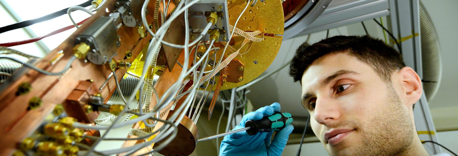 Researcher using a screwdriver to adjust something on a large copper coloured scientific instrument
