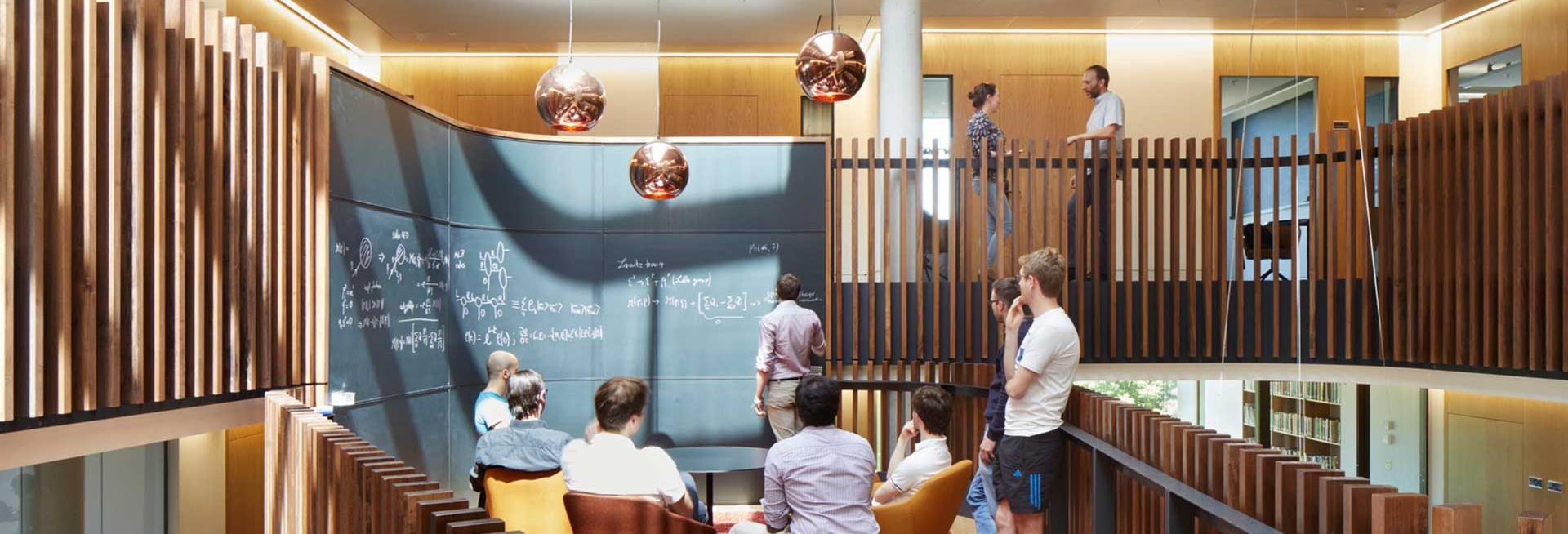 People sitting and standing around a blackboard in the Beecroft Building, Oxford