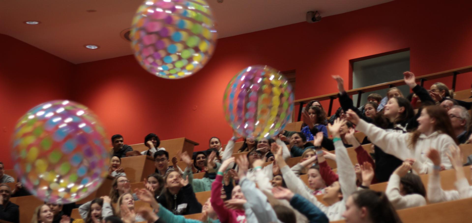 Multicoloured beach balls in the air being pushed around by female students in a lecture theatre