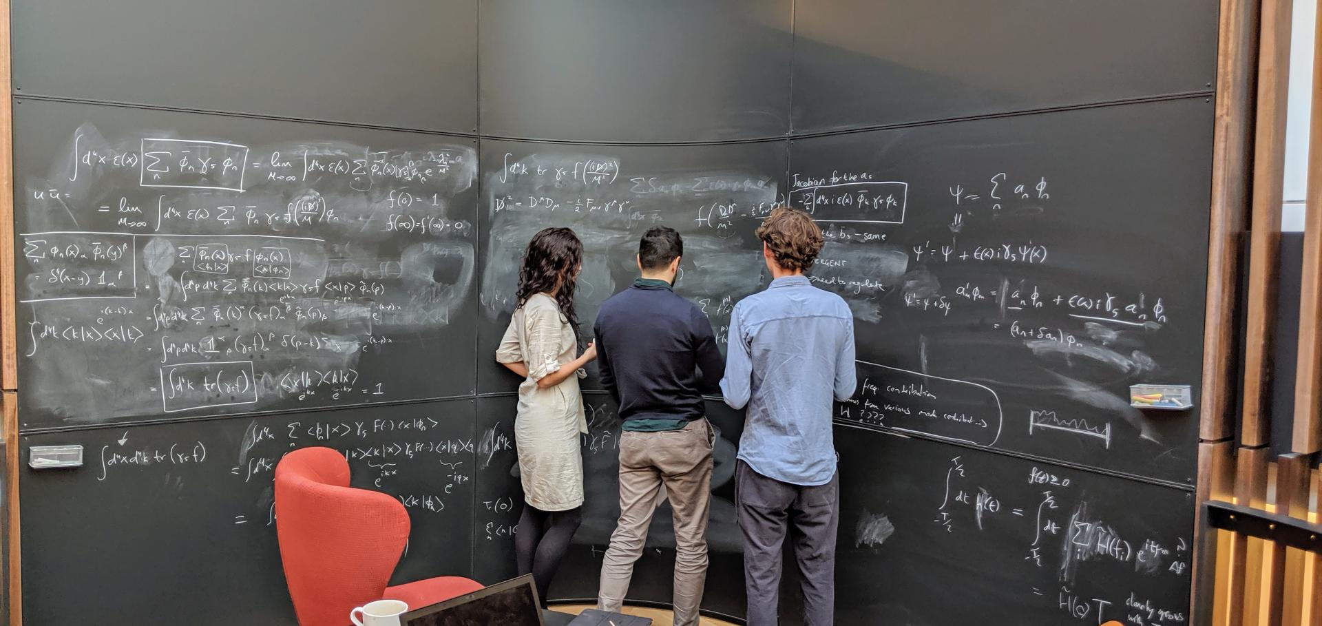 Three physicists standing in front of a blackboard.