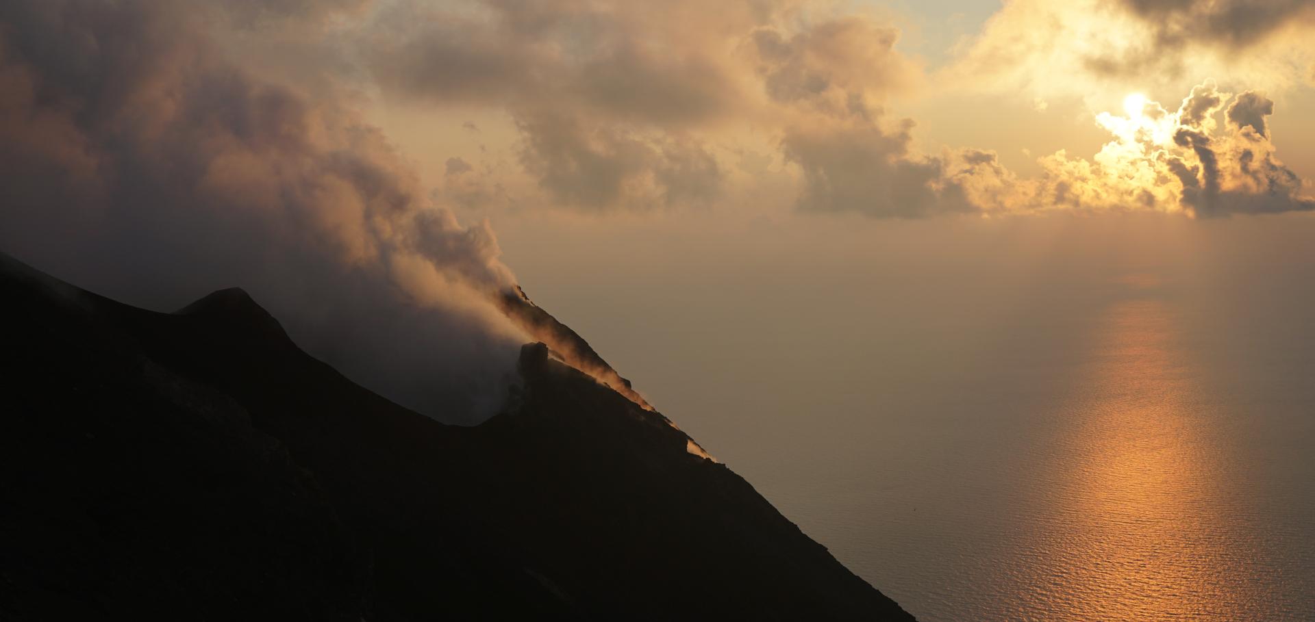 Volcano with sunset in background, over ocean.