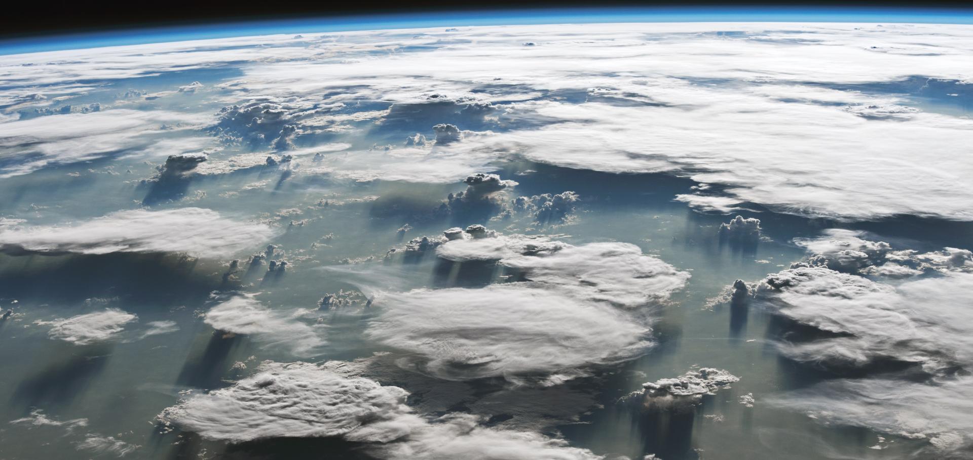 Anvil clouds over the Amazon casting shadows on the green surface below. Photo taken from the ISS, space visible beyond the planet at the top of the image.