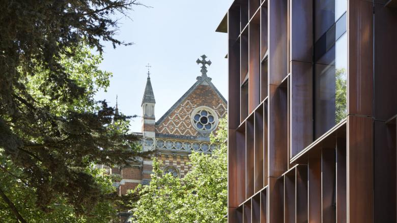 An image of a modern physics building with a tree and an older building  in the background.