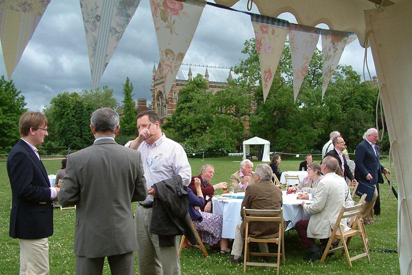 People sitting and standing and chatting in a garden with bunting in the foreground