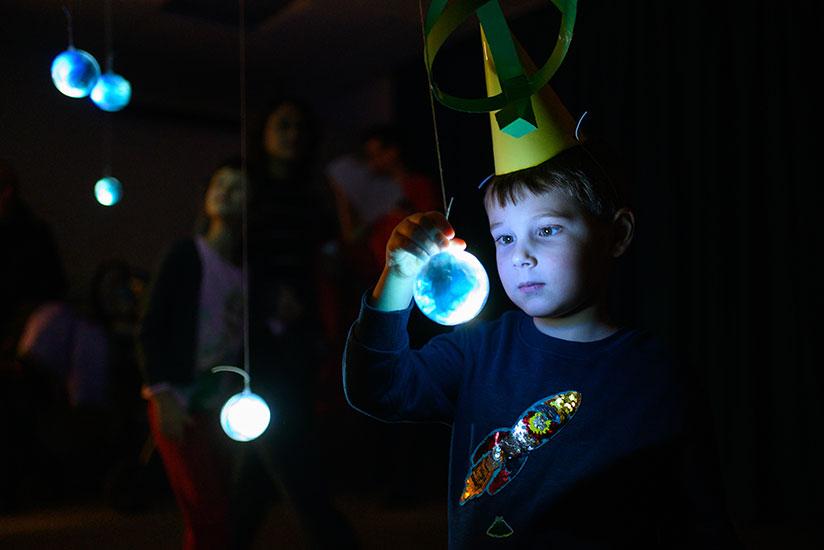 Boy staring at model of planet with a sequin rocket on his jumper