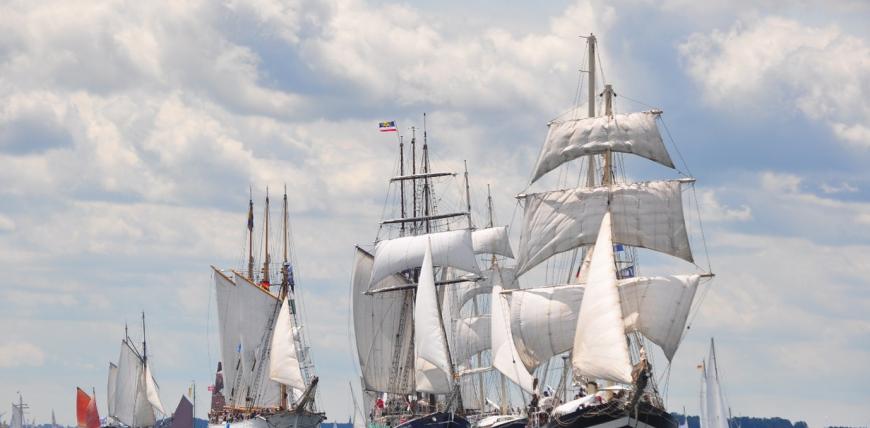 Several traditional sailing ships with full white sails on the water under a cloudy sky during Kiel Week in Kiel, Germany. Tall ships sailing in Kiel Fjord during Kiel Week, which coincided with the visit for the OCCD Colloquium.